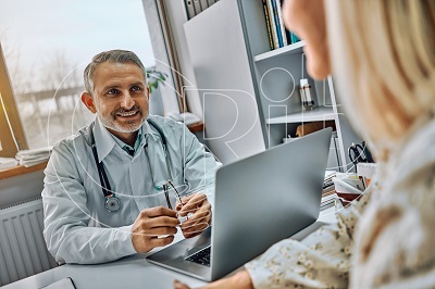 positive emotional practitioner sitting at table in front of happy elderly patient smiling to her